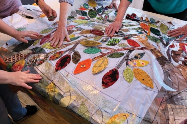 hands touching a quilt with a tree and leaf motif