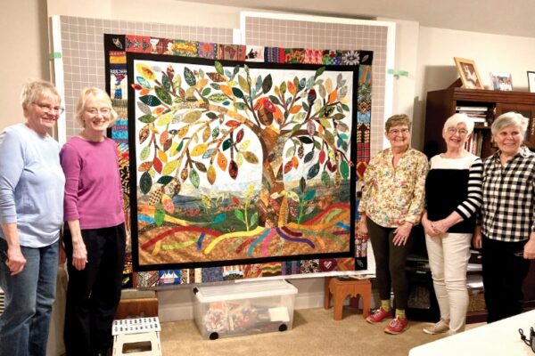 women posing beside a hanging quilt