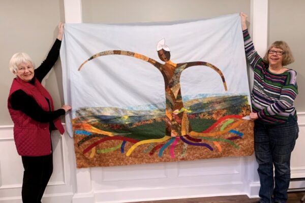 Two women holding up the quilt with a tree motif