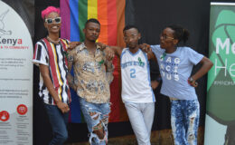 Four young people, members of HAPA, Kenya, posing in front of a rainbow flag