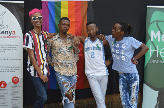 Four young people, members of HAPA, Kenya, posing in front of a rainbow flag